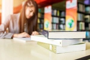 Student at a college library with books in front of her