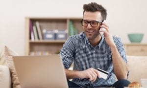 Smiling man activating his credit card on his laptop while on his cell phone