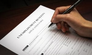 Persons hand holding pen, ready to fill out unemployment benefits form