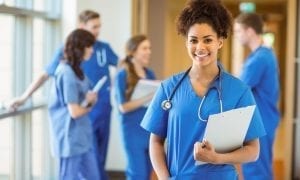 Group of medical students in hallway with girl smiling at camera one hand in pocket, holding clipboard