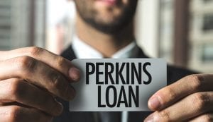 Businessman holding in focus card that says "Perkins Loan" with both hands with out of focus skyscraper window in background