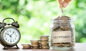 Retro clock next to stacked coins and jar filled with coins labeled retirement on table with depth effect