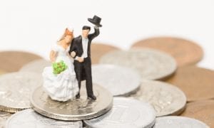 Photo of model bride and groom arm in arm walking on pile of change with groom tipping his hat