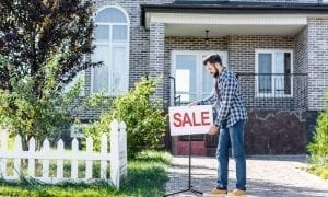 Young male putting up a sale sign in front of his house on walkway