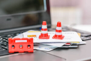 Traffic warning cones atop a stack of credit cards on a laptop, depicting not using cards in consolidation.